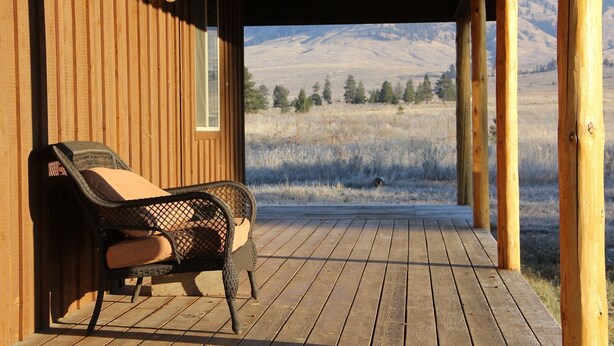 A wooden deck with a single wicker chair and a window overlooking a mountainous landscape. - Ranch Style Cabin on 20 Acres in the Beautiful Tunk Valley (Riverside)