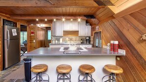 Una cocina moderna con detalles de madera, una isla central con taburetes y un refrigerador de acero inoxidable.