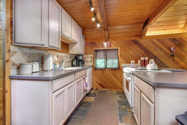 A kitchen with white cabinets, a stone backsplash, and a wooden ceiling.