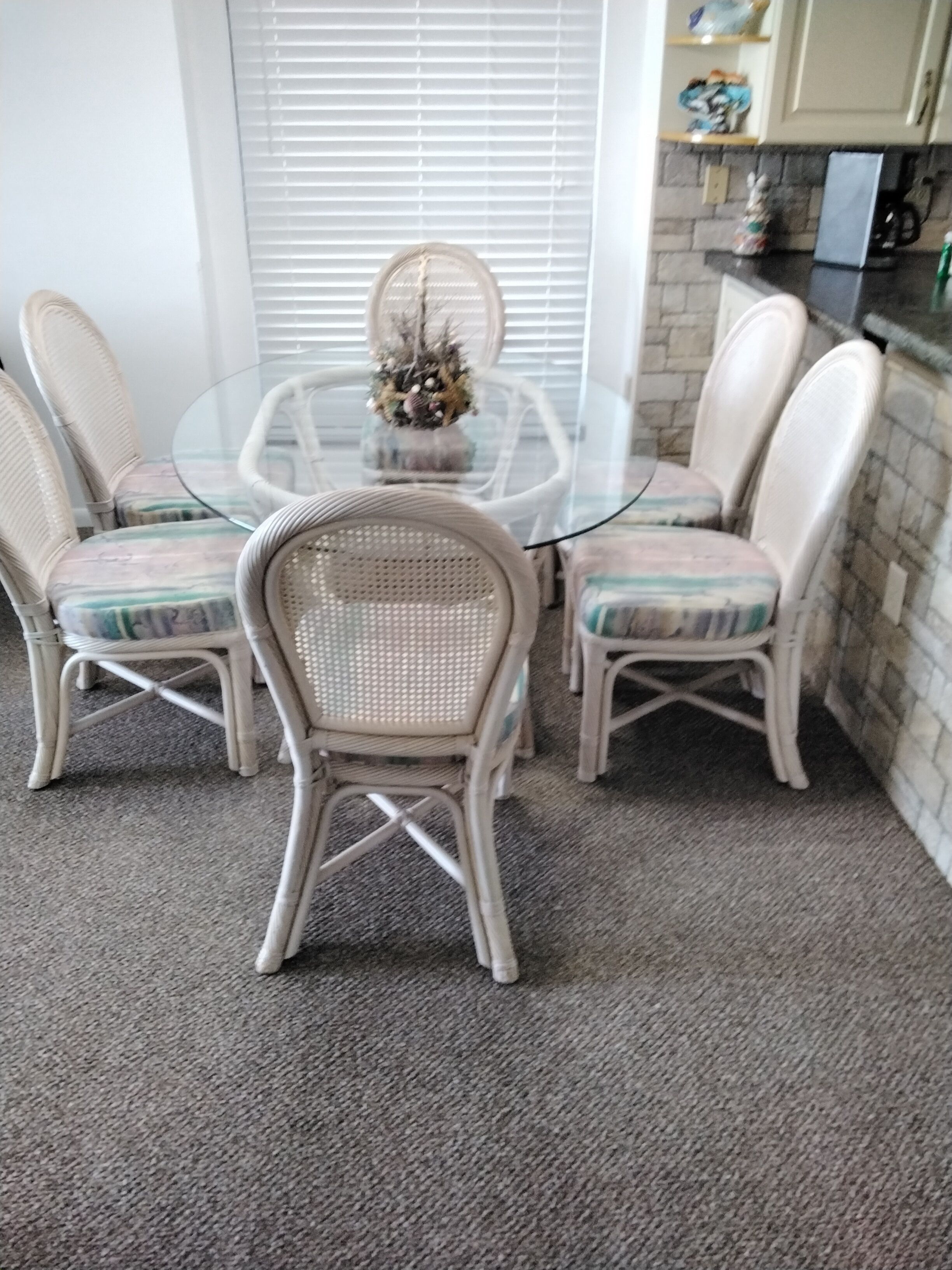 A dining area with a glass table surrounded by wicker chairs with cushioned seats.