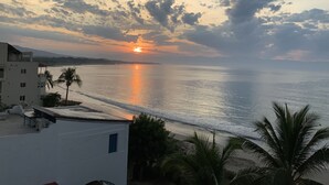 A coastal view with a sunset, calm sea, and buildings with balconies.