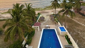 A pool with a view of the beach and ocean, surrounded by palm trees and lounge chairs.