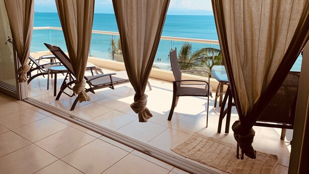 A balcony with a view of the ocean, featuring two lounge chairs and a table.