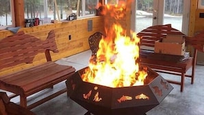 En eldstad med flammor i en utomhusmiljö med träinredning och sittplatser.