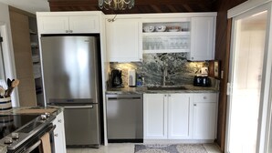 Eine kompakte Küche mit einem Edelstahl-Kühlschrank, einem Geschirrspüler und einer Kaffeemaschine. Weiße Schränke und einer Marmor-Spritzschutz sind vorhanden.