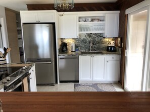 A compact kitchen with a stainless steel refrigerator, a dishwasher, and a coffee maker. There are white cabinets and a marble backsplash. - Hale Maluhia - 2 Minutes from the Big Island's Best Beaches (Kamuela)