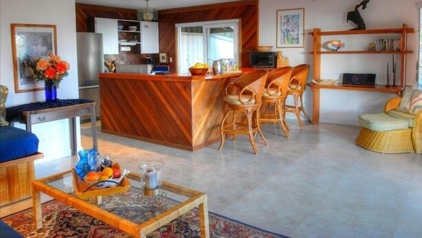 Eine moderne Küche mit einer zentralen Kochinsel, Holzstühlen, einer Essecke mit einer Couch und einem Bücherregal.