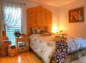 A bedroom with a bed, a nightstand, a lamp, a window with sheer curtains, and a framed picture on the wall. - Hale Maluhia - 2 Minutes from the Big Island's Best Beaches (Kamuela)