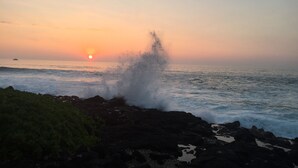 Ein Sonnenuntergang über einer felsigen Küste, Wellen schlagen an den Felsen