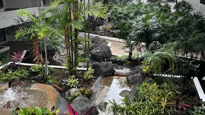 Ein mehrstöckiger Innenbereichsgarten mit Wasserspiel, verschiedenen tropischen Pflanzen und einem Kiesweg.