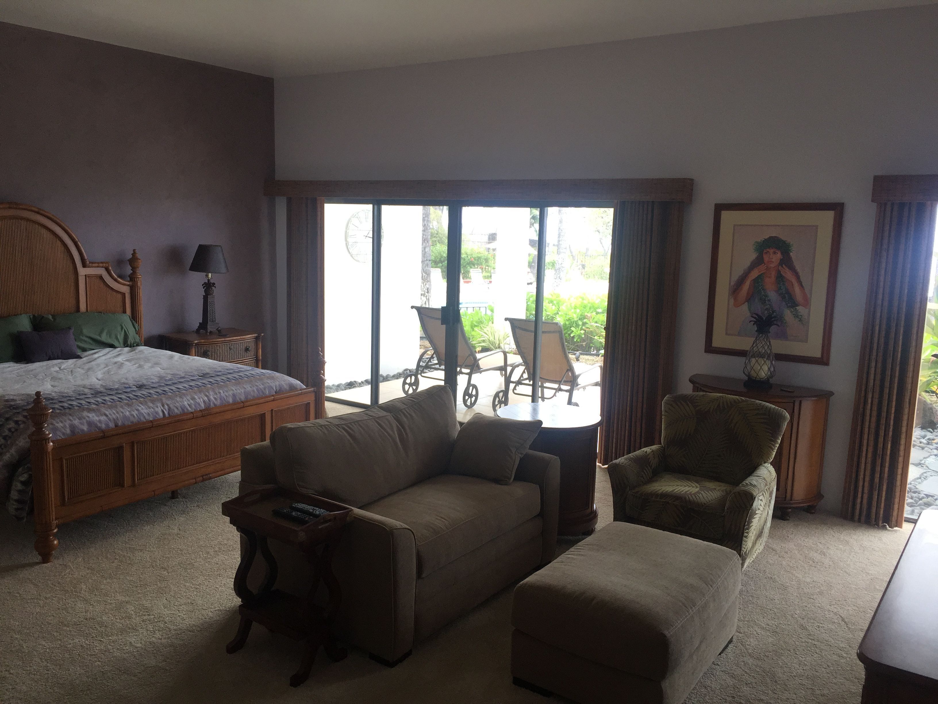 A hotel room with a bed, a sofa, a chair, a small table, and a painting on the wall.
