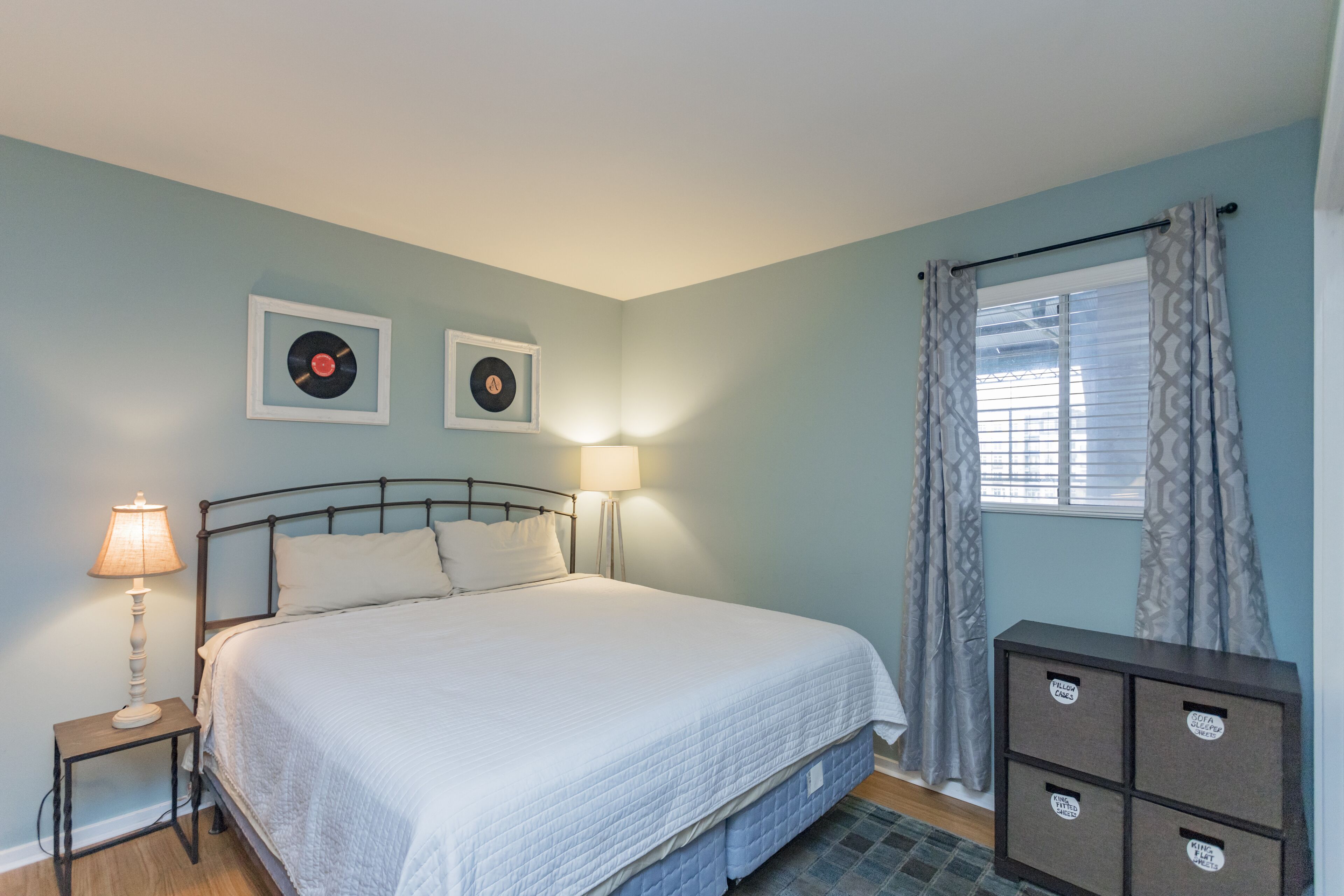 A bedroom with a bed, bedside lamps, a dresser, and two framed records on the wall.