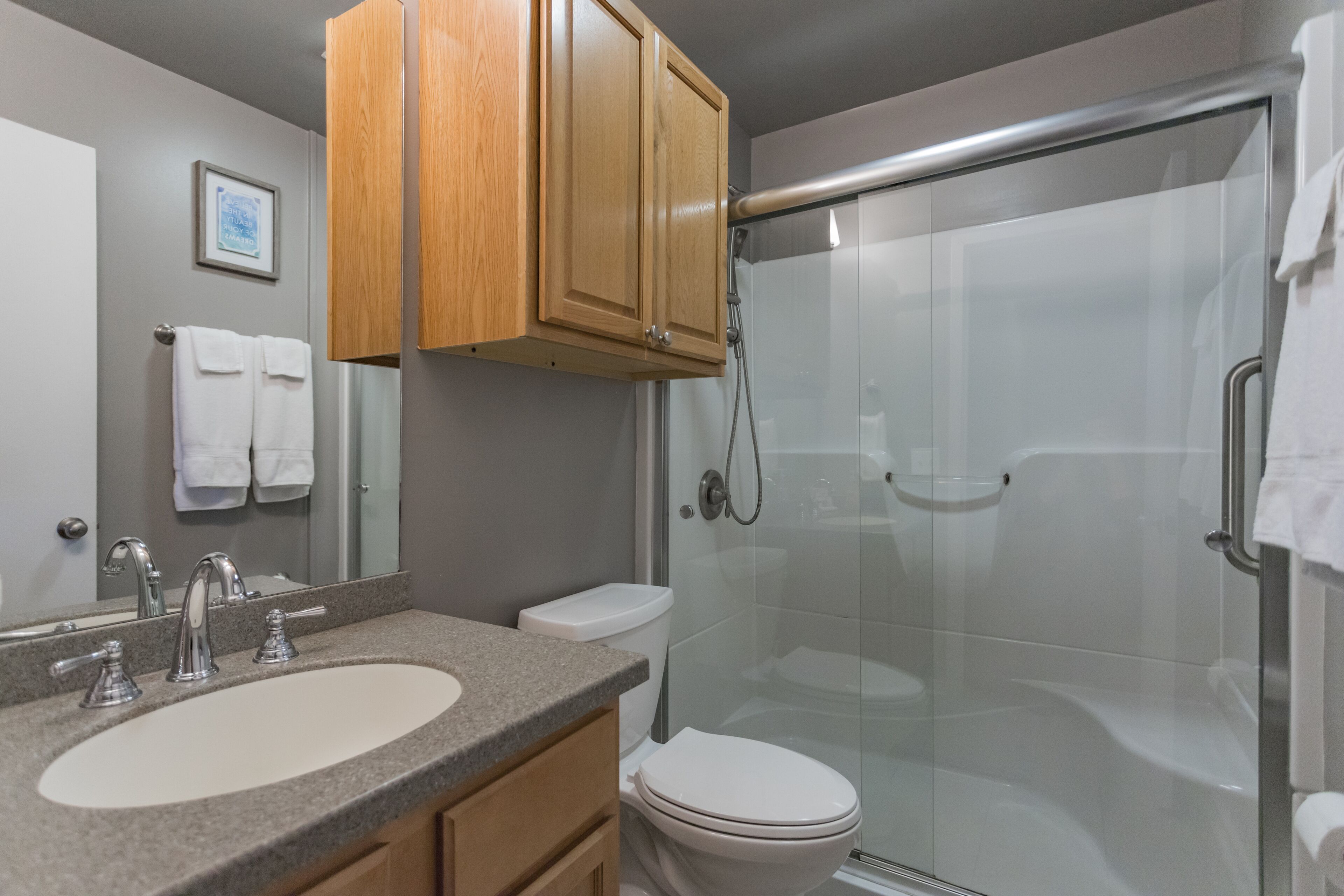 A modern bathroom with a granite countertop sink, a white toilet, and a glass-enclosed shower.