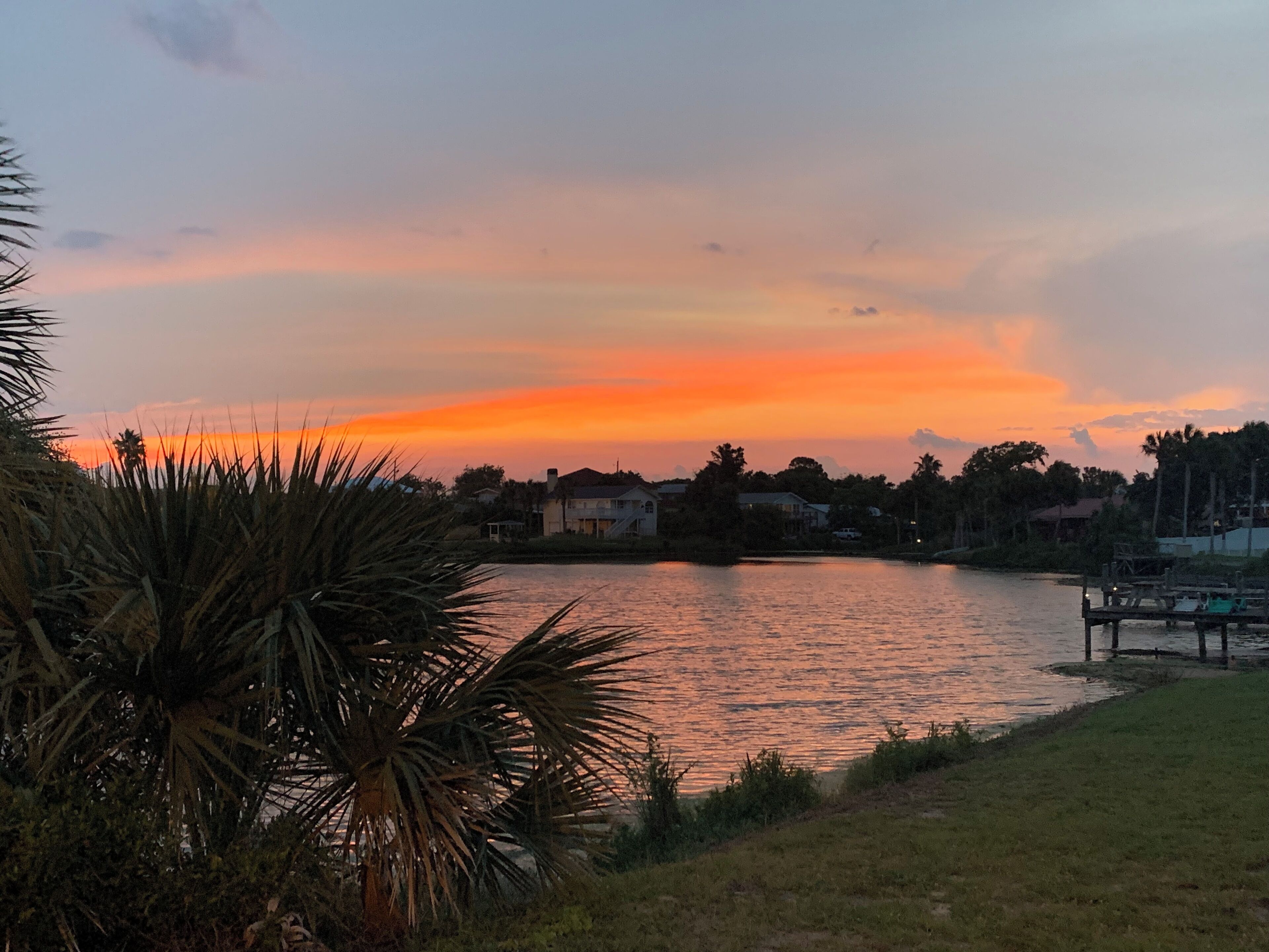 A sunset over a calm lake with houses and palm trees in the foreground.