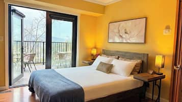 A hotel room with a large bed, two bedside tables with lamps, a balcony with chairs, and a large floral artwork on the wall.
