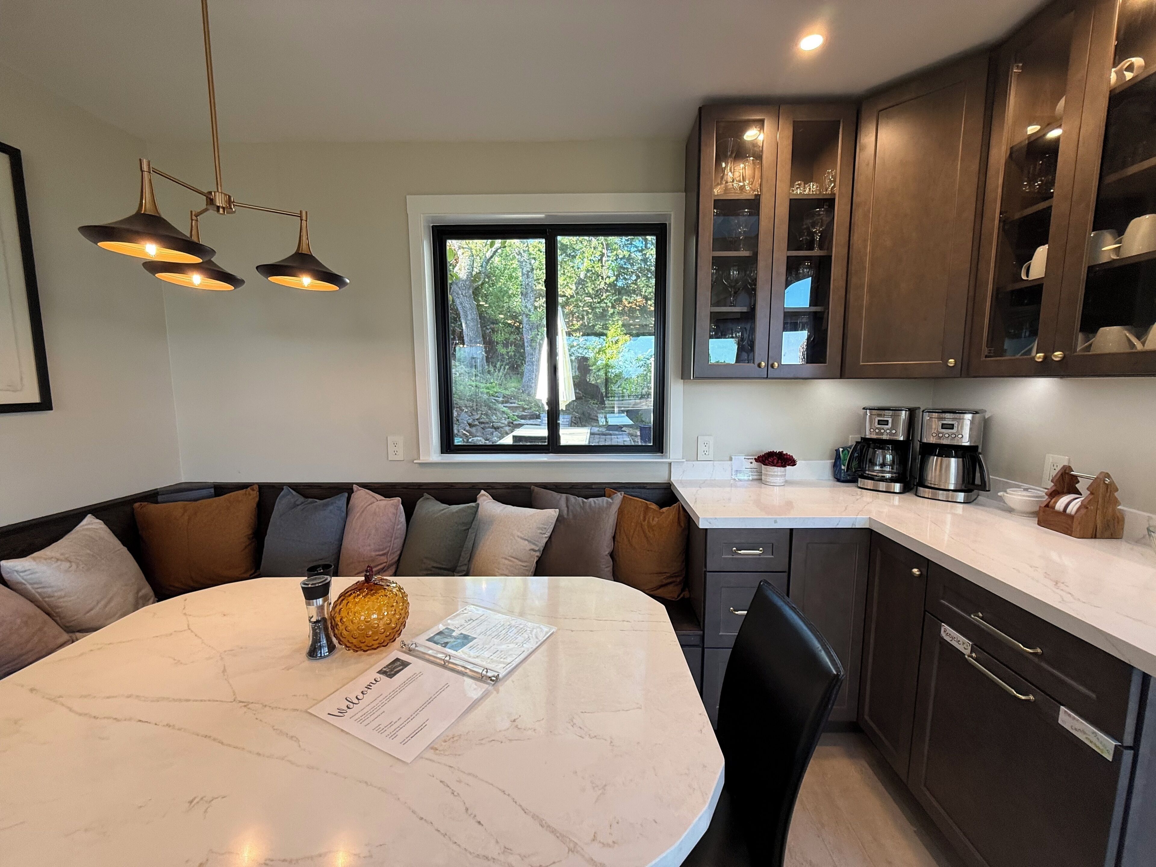 Cocina moderna con una isla de mármol, gabinetes de madera oscura y un ventanal con vista a la vegetación.
