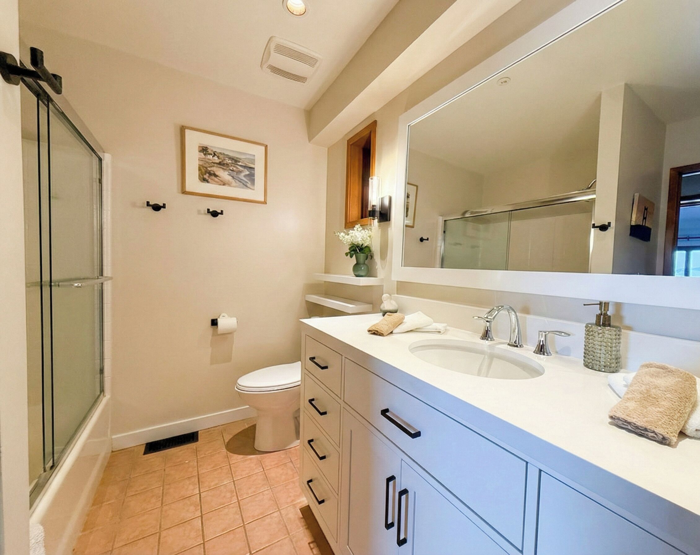 A modern bathroom with a large mirror, white sink, and a shower enclosure.
