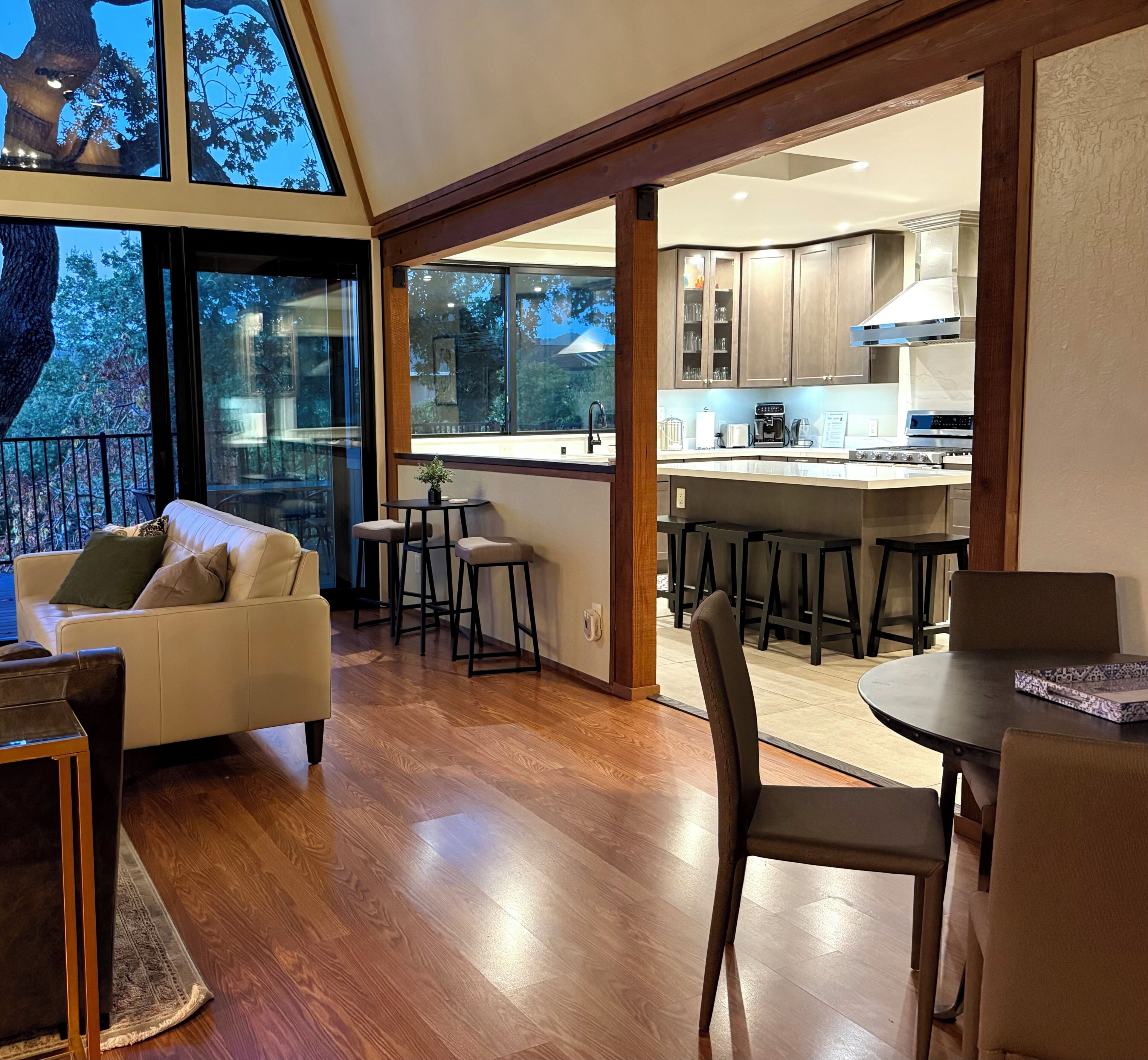 A modern interior with a dining area, kitchen, and a large window overlooking a tree.