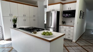 Une cuisine moderne avec des meubles blancs, un réfrigérateur en acier inoxydable, un four encastré et un îlot central sur lequel se trouve un saladier rempli de pommes vertes.