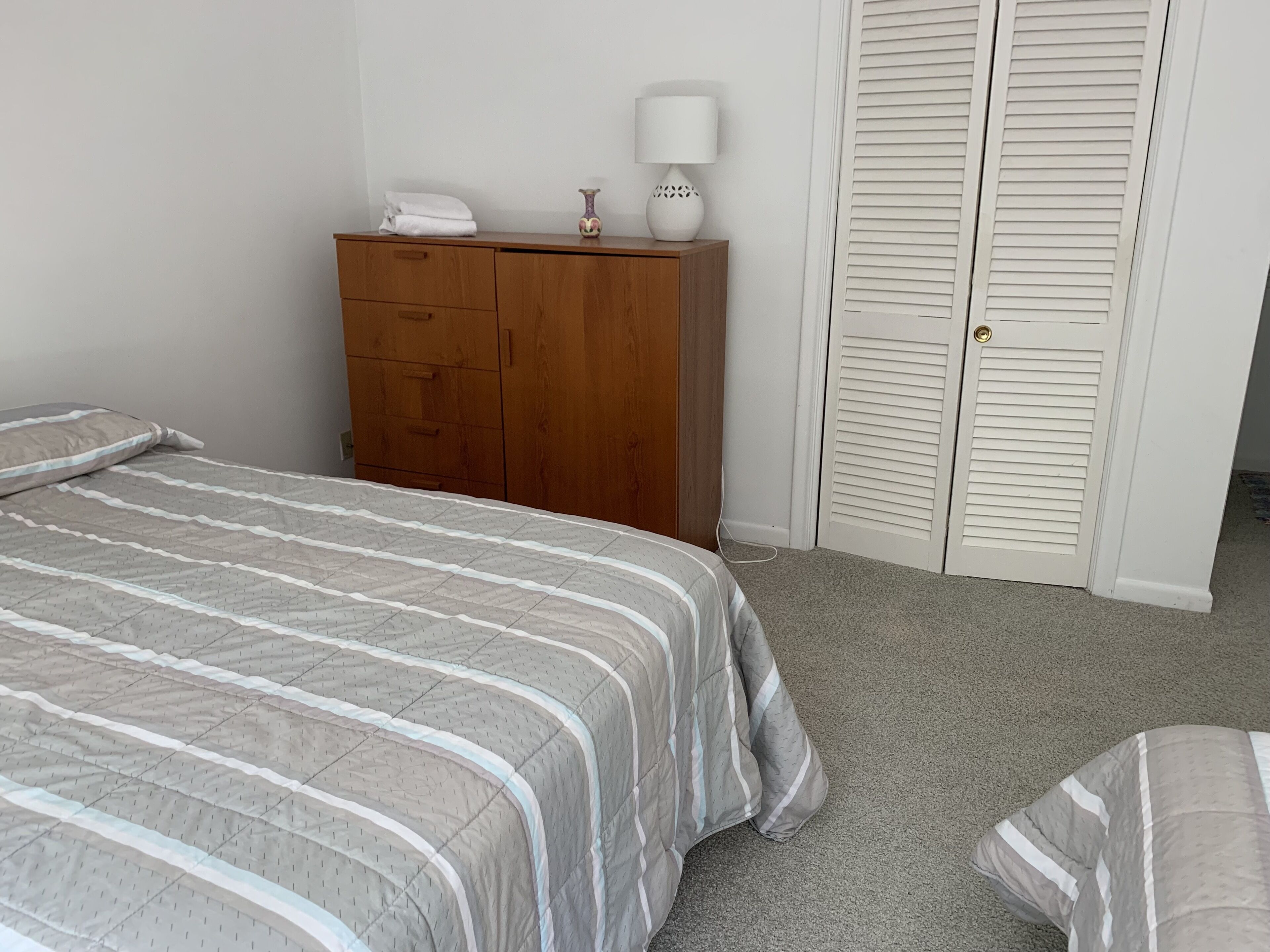 A bedroom with a bed, a wooden dresser, a lamp, and a closet.