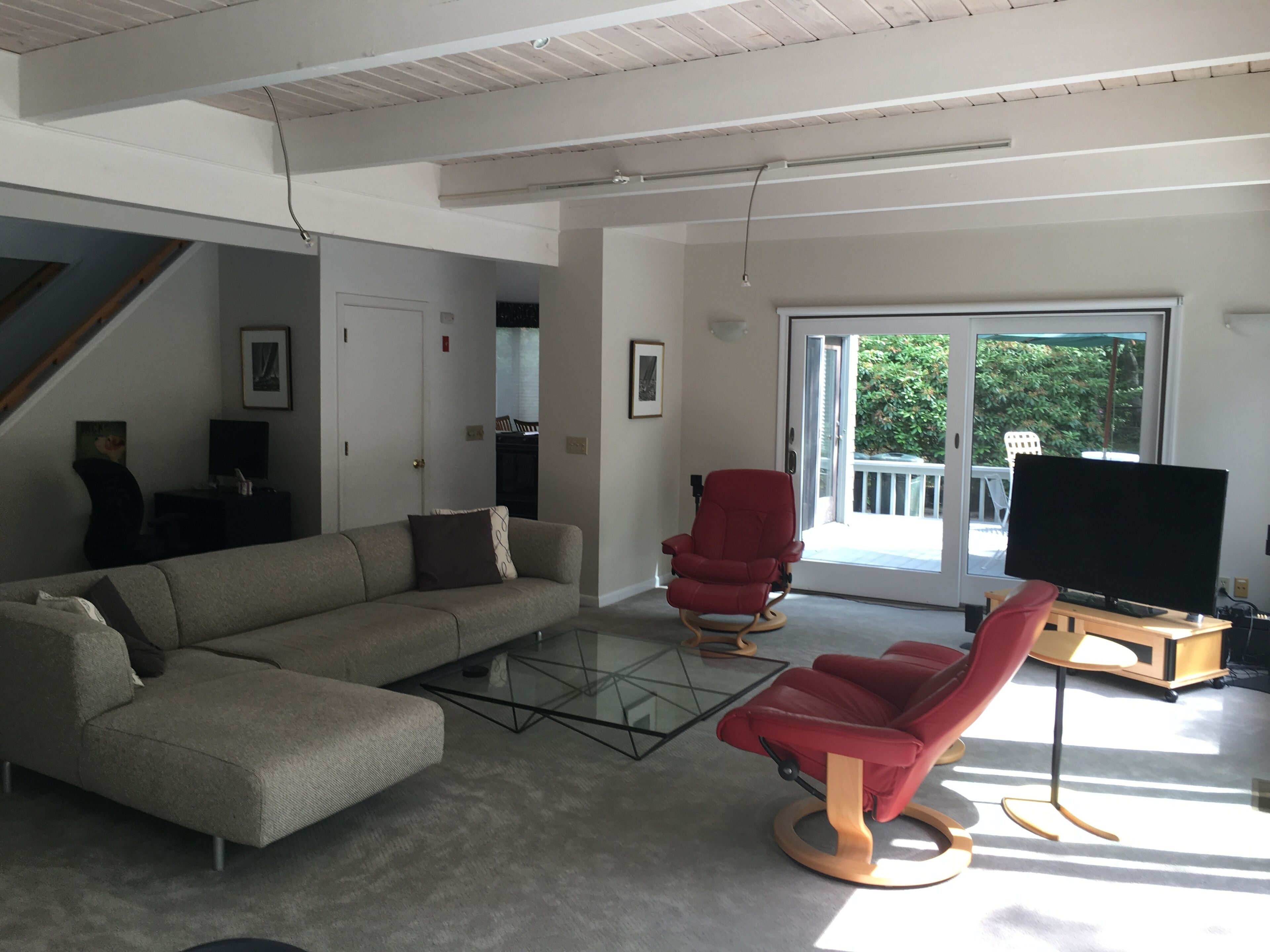 A modern living room with a sectional sofa, a red armchair, a glass coffee table, and a flat-screen TV on a wooden stand.