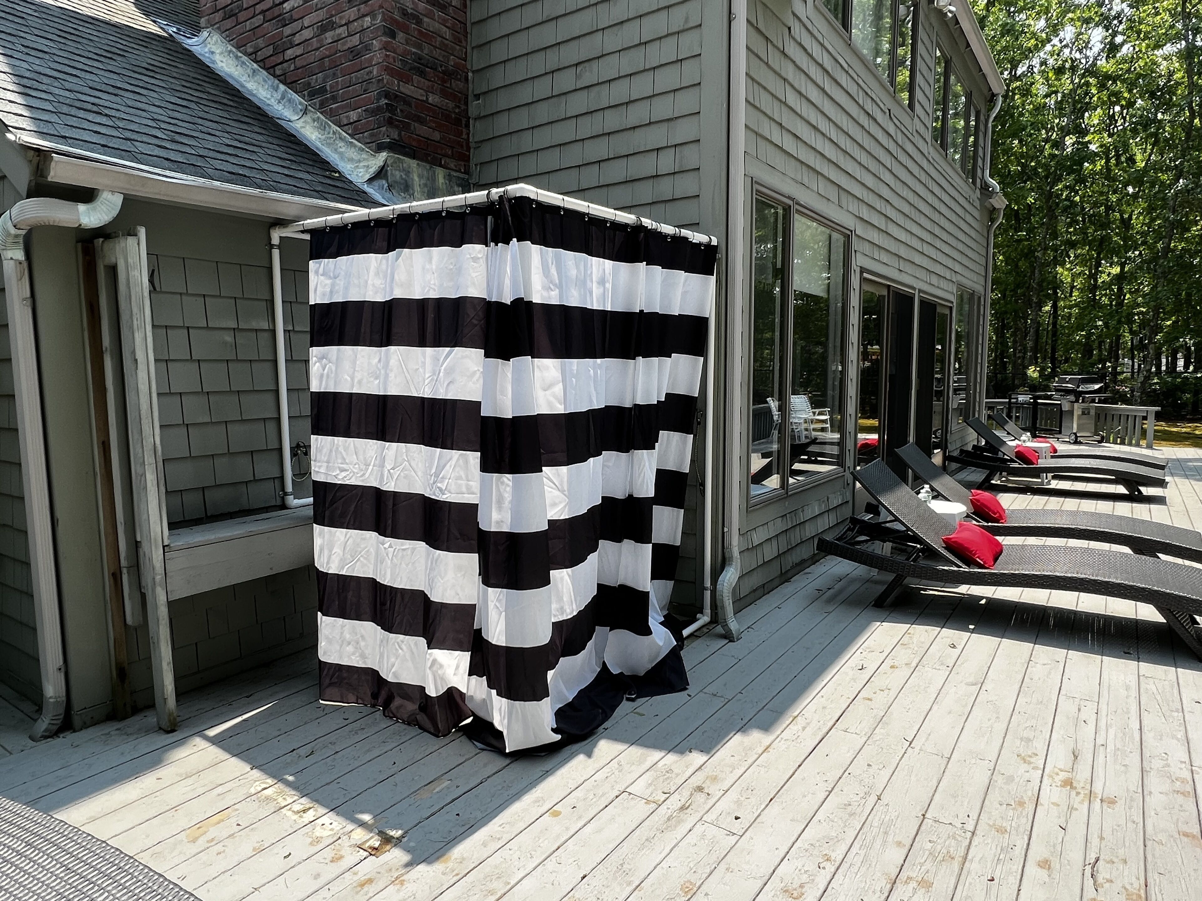 A covered outdoor seating area with a striped awning, a wooden deck, and a glass door leading to a patio.