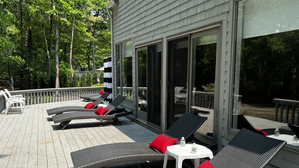 Une terrasse dotée de fauteuils de jardin en osier et de coussins rouges, d’une petite table avec une bouteille, et offrant une vue sur les arbres environnants.
