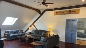 A modern living room with a loft-style ceiling, wooden beams, and a sign for Sunflour TeaRoom offering soups, salads, sandwiches, and desserts. - Recently Renovated In-Town Bar Harbor 4 Bed 3 Bth Apartment with Private Parking (Bar Harbor)