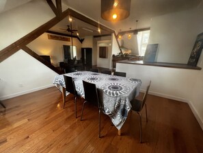 Ein Essbereich mit einem Tisch, der mit einer gemusterten Tischdecke bedeckt ist, Holzstühle und einem Deckenventilator.