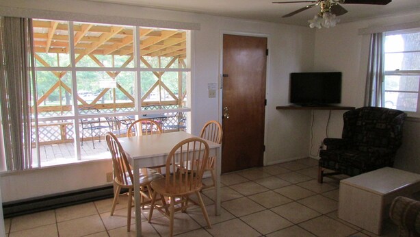 A room with a dining table and chairs, a television on a stand, and a door. - Come stay in our 2bd cabin on Table Rock Lake close to Silver Dollar City! (Branson)
