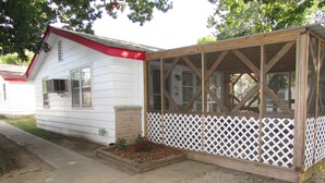 A small, single-story house with a red roof and white siding, featuring a wooden porch with lattice railings. - Come stay in our 2bd cabin on Table Rock Lake close to Silver Dollar City! (Branson)