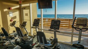 A gym with cardio machines and a large window overlooking the beach.