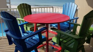 Un balcón con una mesa roja y sillas de colores, con vistas a la playa.
