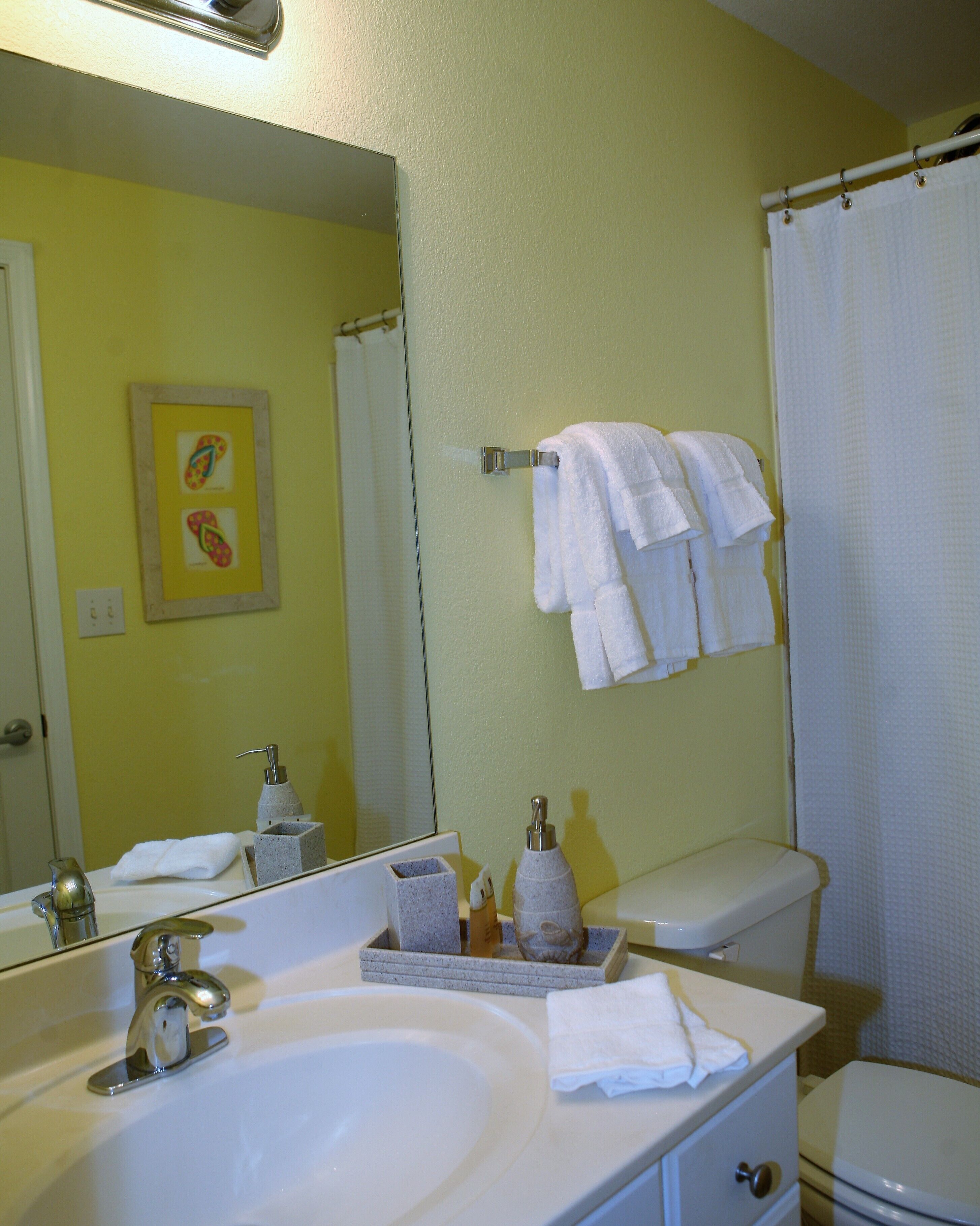 A bathroom with a sink, mirror, toilet, and shower curtain.
