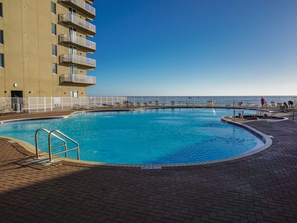 A swimming pool with a clear view of the ocean, surrounded by a brick walkway and a white fence.