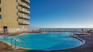 Una piscina con vista despejada al océano, rodeada por un paseo de ladrillo y una valla blanca.
