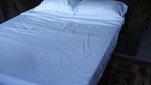 Ein Bett mit weißer Bettwäsche in einem Raum mit Teppichmuster und einem Holz-Kopfteil.