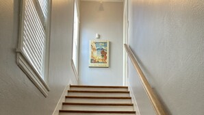 Una scala con gradini in legno e pareti bianche che conduce a un pianerottolo con un quadro incorniciato.