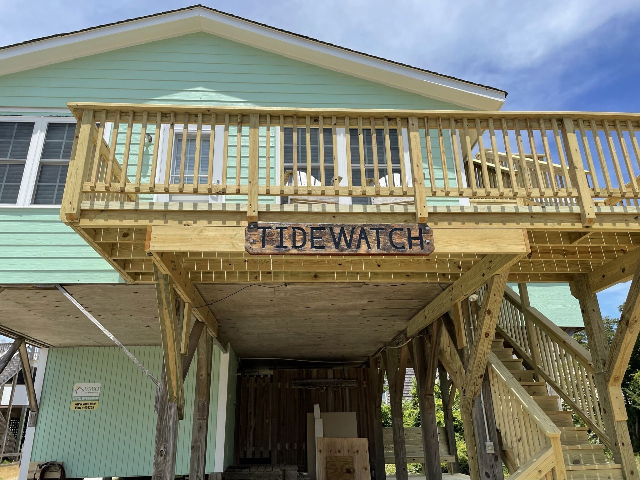 Una terraza de madera con un letrero que dice "Tide Watch" sobre un edificio de fachada verde.