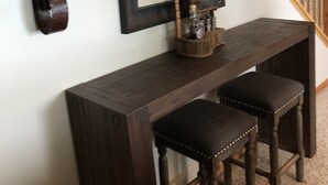 A dark wooden console table with two barstools, a framed picture above, and decorative wall sconces.