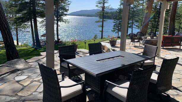 An outdoor patio with a stone floor, wicker chairs, a table, and a view of a lake and mountains.