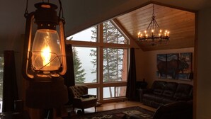 A cozy living room with a large window, a chandelier, and a lit lantern.