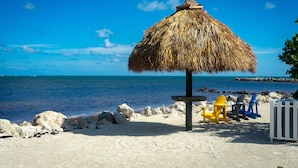 Una playa con un paraguas de paja, una mesa y sillas de colores.