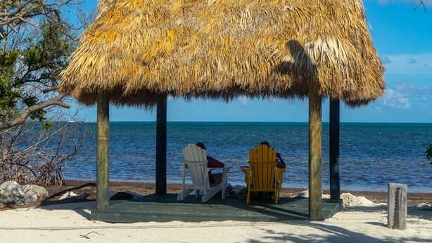 A thatched-roof structure with two chairs under it, overlooking a beach and the sea.
