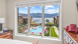 A room with a large window overlooking a swimming pool, outdoor seating, and a mountainous landscape. -  Luxury Beachfront Penthouse Suite. Approved for short-term rentals. (West Kelowna)