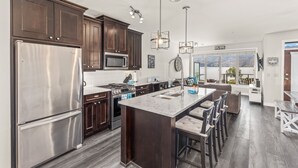 A modern kitchen with dark wood cabinets, stainless steel appliances, and a large island with bar stools. -  Luxury Beachfront Penthouse Suite. Approved for short-term rentals. (West Kelowna)