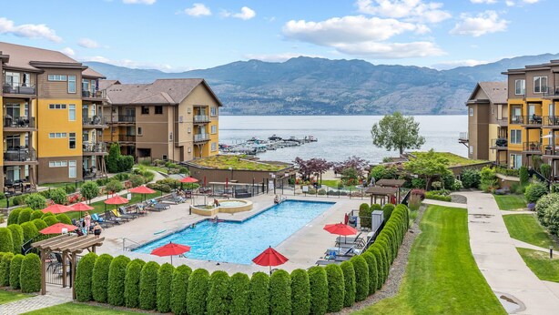 A residential building with a swimming pool, surrounded by well-maintained lawns and a view of a lake with mountains in the background. -  Luxury Beachfront Penthouse Suite. Approved for short-term rentals. (West Kelowna)