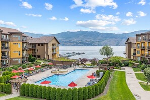 A residential building with a swimming pool, surrounded by well-maintained lawns and a view of a lake with mountains in the background. -  Luxury Beachfront Penthouse Suite. Approved for short-term rentals. (West Kelowna)