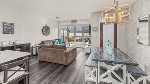 A modern living room with a large window, a cozy seating area, and a dining table. -  Luxury Beachfront Penthouse Suite. Approved for short-term rentals. (West Kelowna)