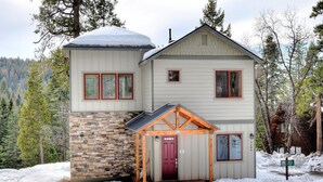 Eine zweistöckige Lodge mit Steinverkleidung und roter Tür, umgeben von Schnee und Bäumen.